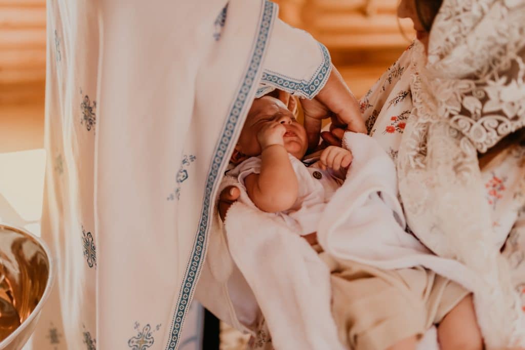 rite of sacrament of epiphany child baby in church. priest blesses child, smears with holy water, puts on a cross.